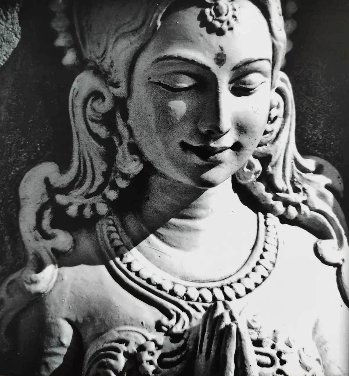 Black and white close-up of a serene statue with eyes closed and hands in prayer